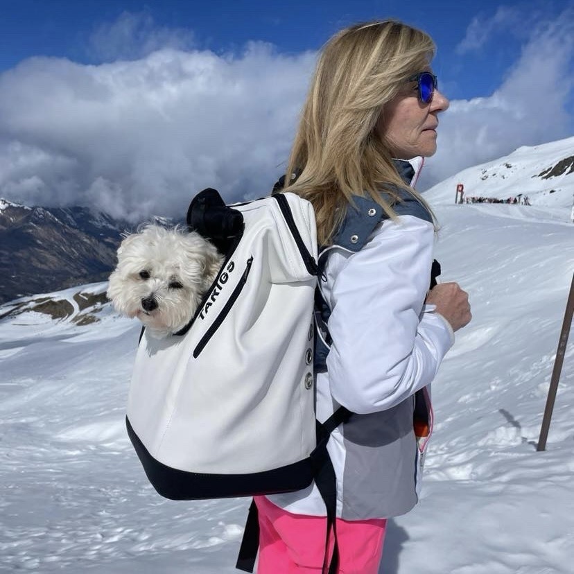 Woman carries the MountainRock Backpack - Medium, White (Vegan Leather) on her back in the ski area. A 9-year-old Coton de Tulear sits in the dog backpack.