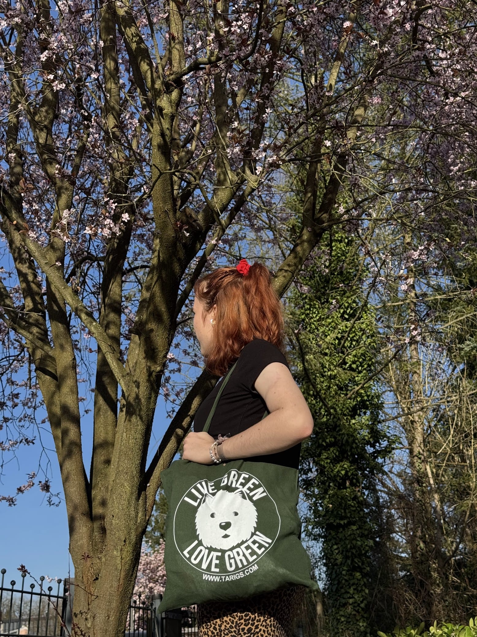 Woman with green TARIGS cloth bag with “LIVE GREEN, LOVE GREEN” print standing under a tree outdoors.